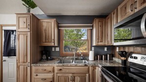 A kitchen with wooden cabinets, a granite countertop, a stainless steel sink, and a built-in oven. - Mountain cabin w/ hot tub & game room (Romney)