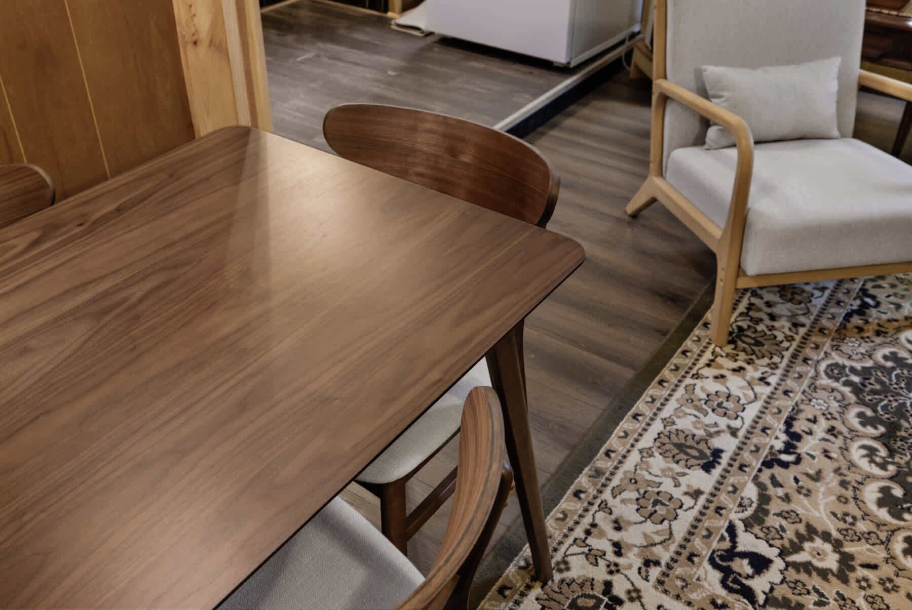 Una mesa de madera con sillas, un tapete estampado y un armario blanco al fondo.