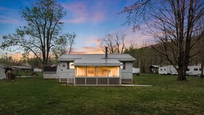 A small, single-story house with a porch, surrounded by a grassy yard and trees. - Wood Stove, Fire Pit, Kayaks - 2 Min Walk to River (Springfield)