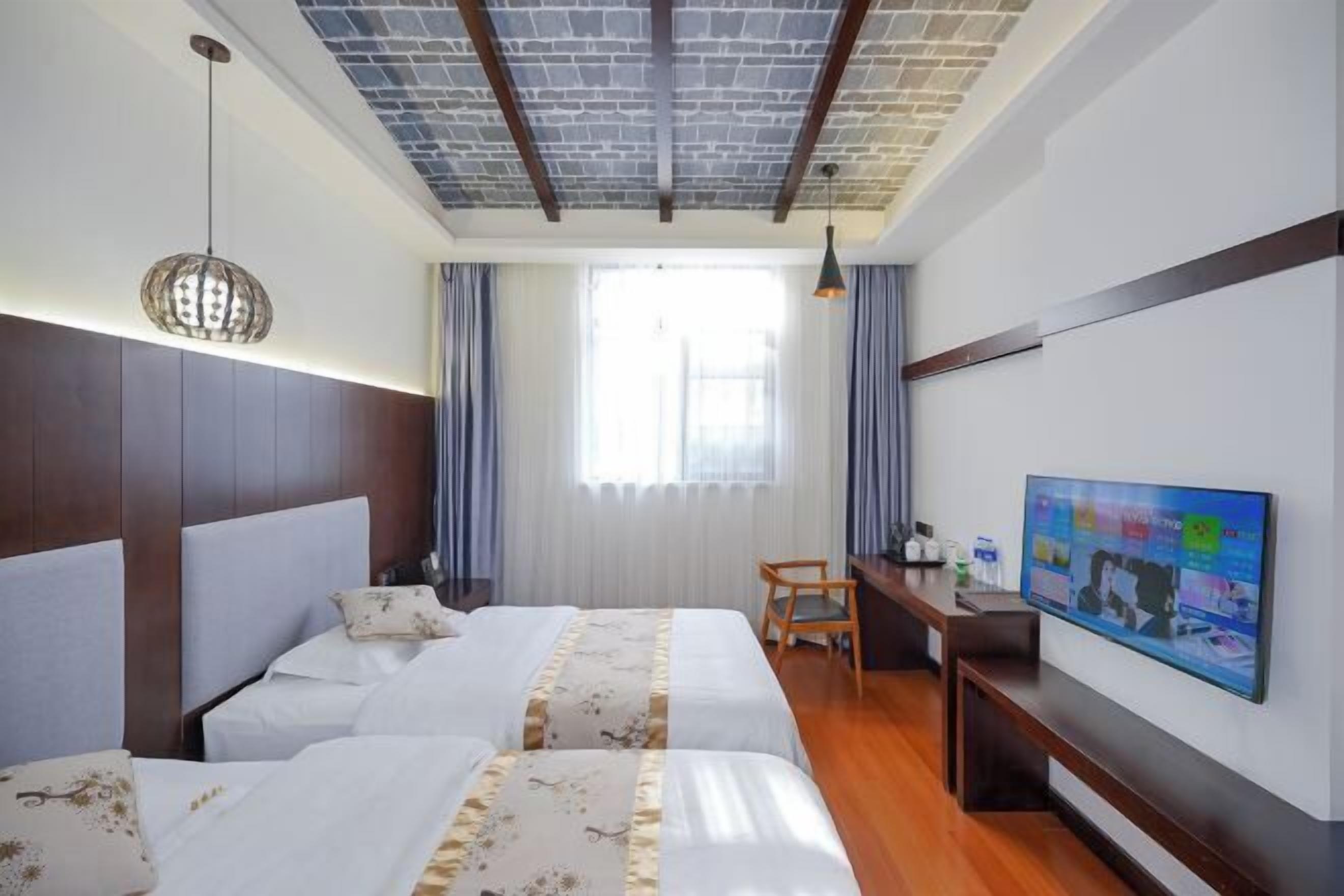 A hotel room with two beds, a desk, a television, and a window with curtains.