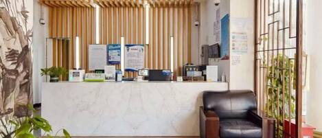 A reception area with a wooden slatted ceiling, a reception desk, a leather chair, and a potted plant.