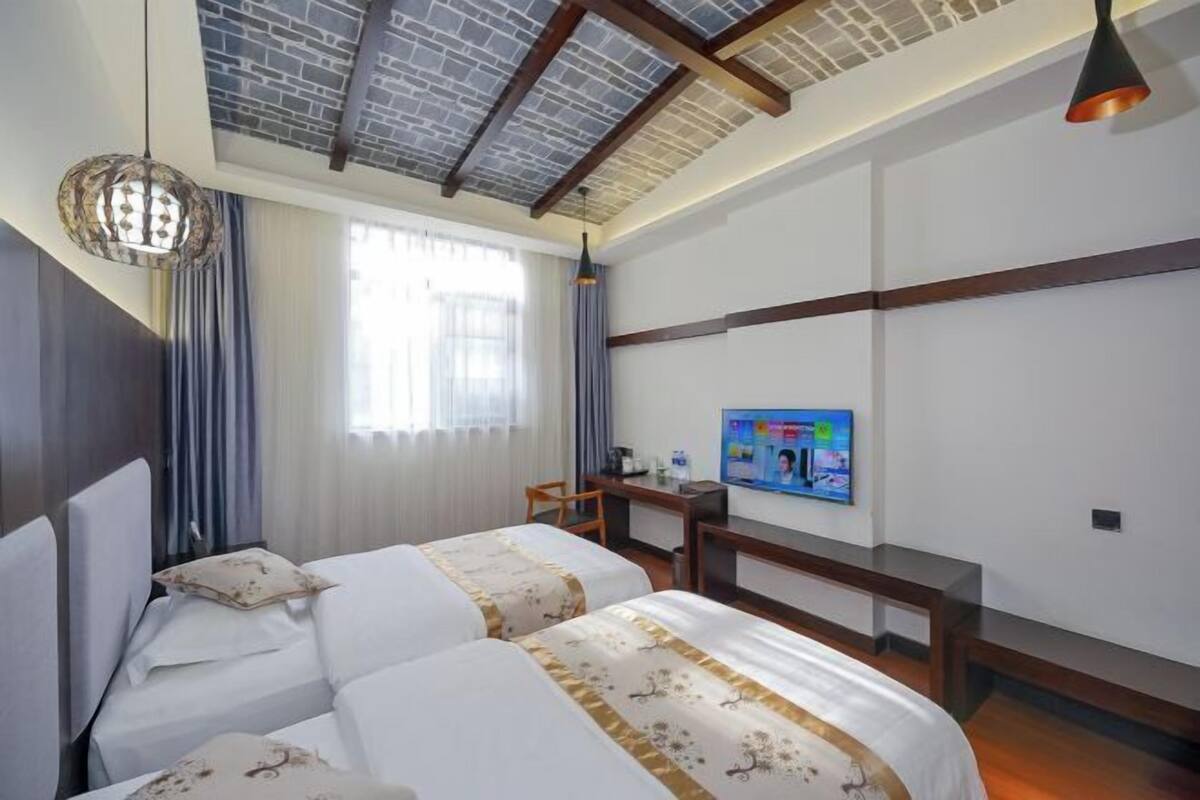 Ett hotellrum med två sängar, en tv, ett skrivbord och ett tak med synliga takbjälkar.