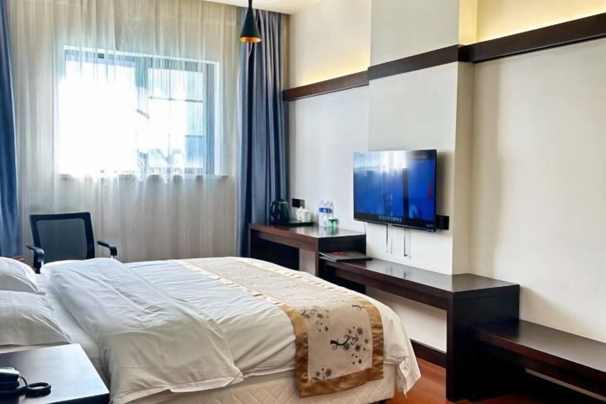 Ett hotellrum med en säng, ett skrivbord, en stol, en tv och ett fönster med gardiner.