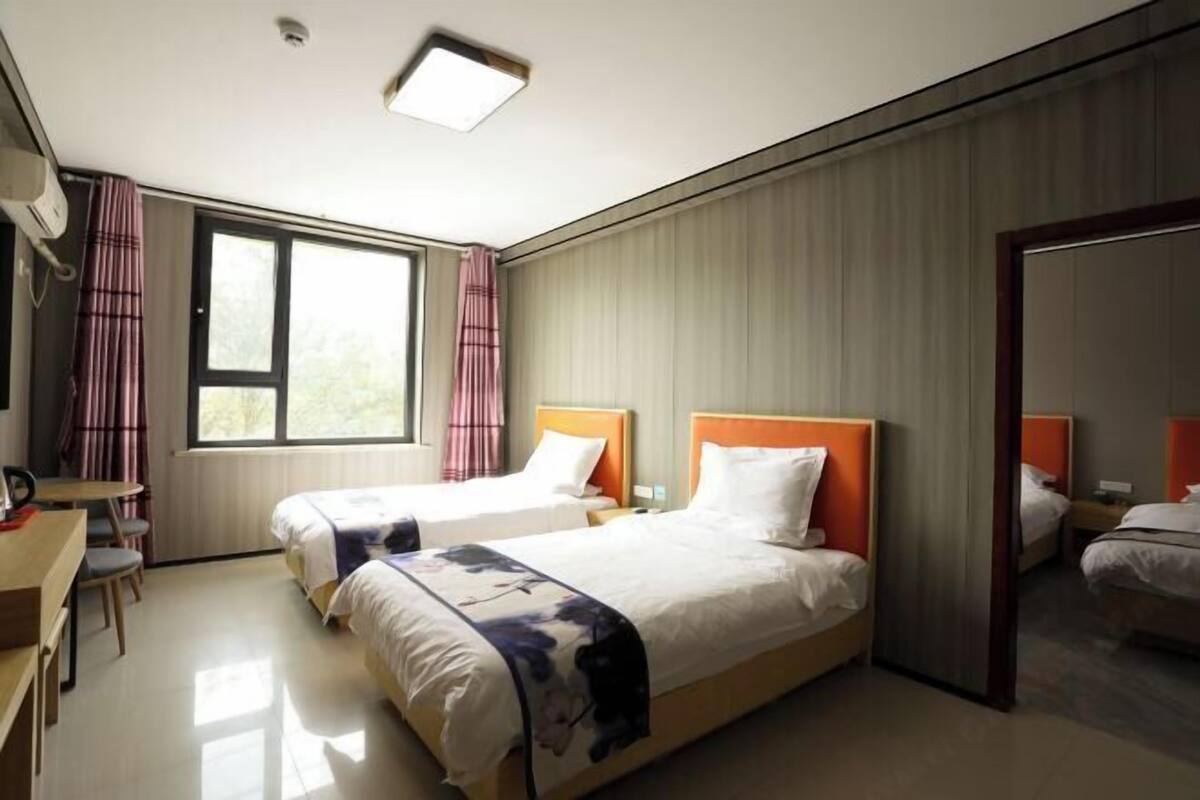 Une chambre d’hôtel avec deux lits, un bureau, une chaise, une fenêtre avec des rideaux et un miroir.