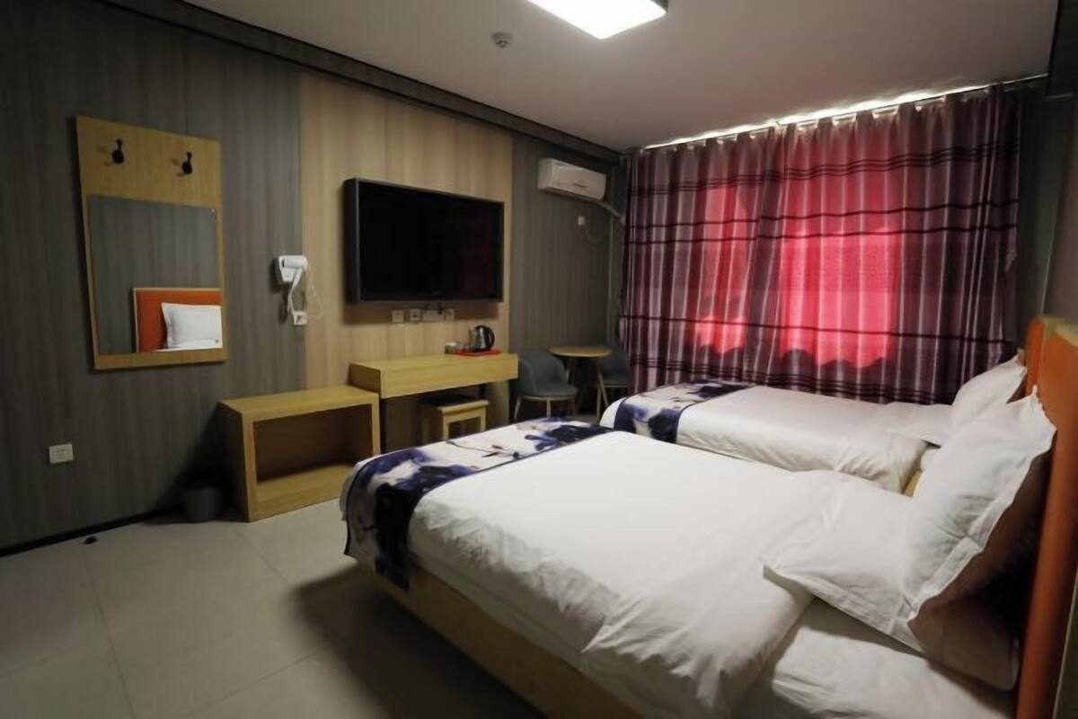 Une chambre d’hôtel avec deux lits, une télévision, un bureau, une chaise, un banc et une fenêtre avec des rideaux.