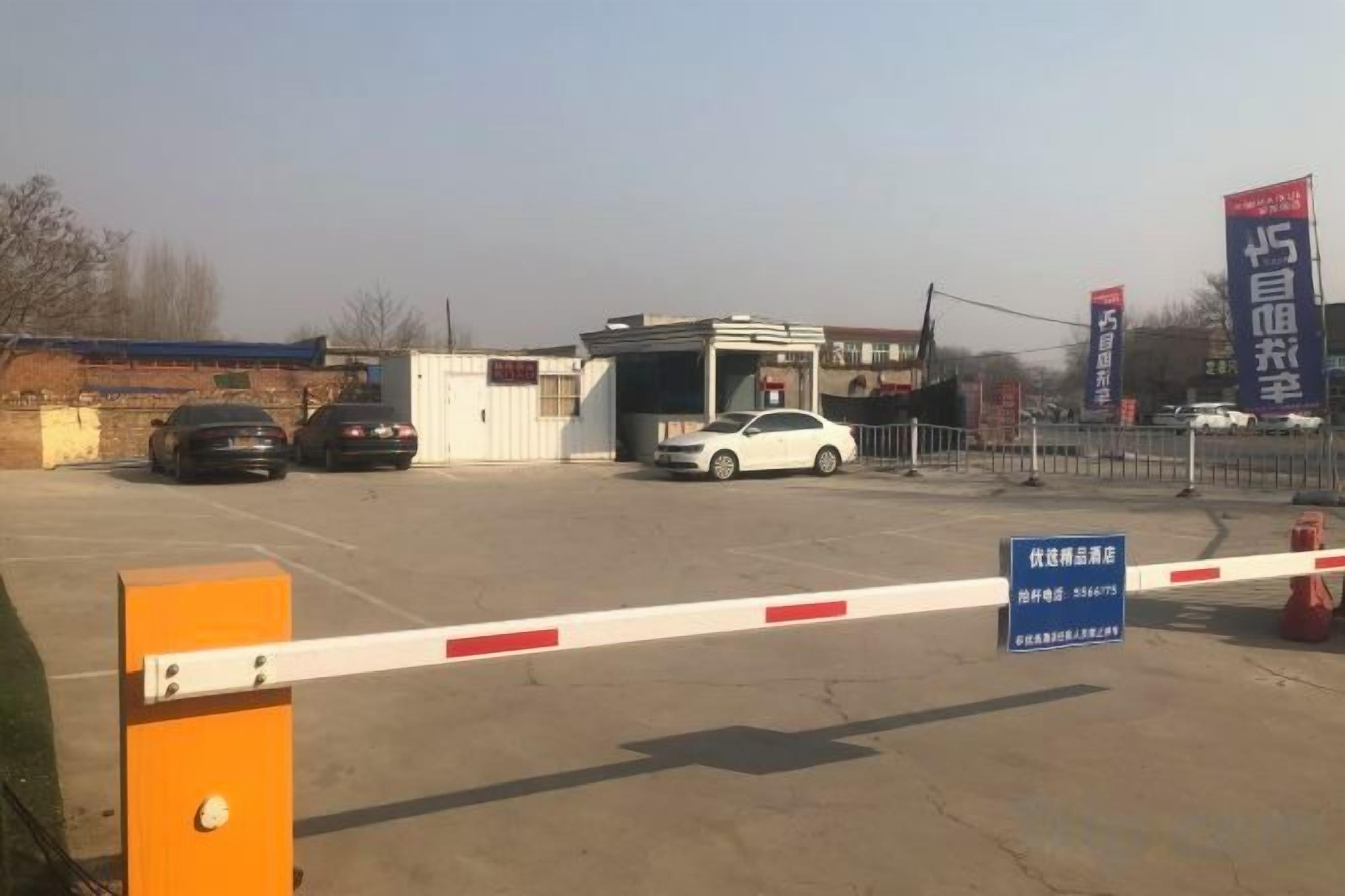 A gated entrance with a barrier, a small building, and parked cars.