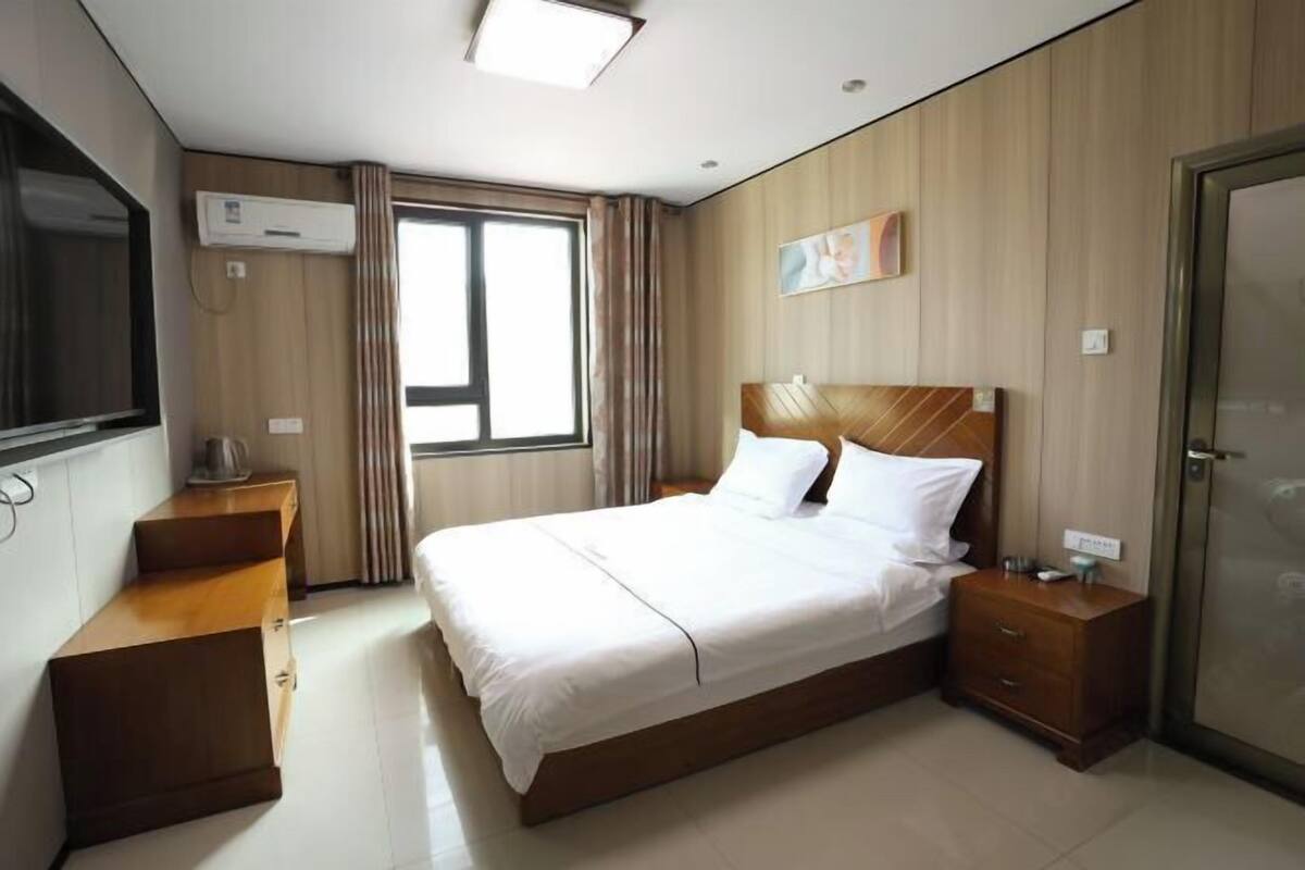Une chambre d’hôtel comprenant un lit, des tables de chevet, un bureau, un appareil de climatisation, une fenêtre avec des rideaux et une porte.