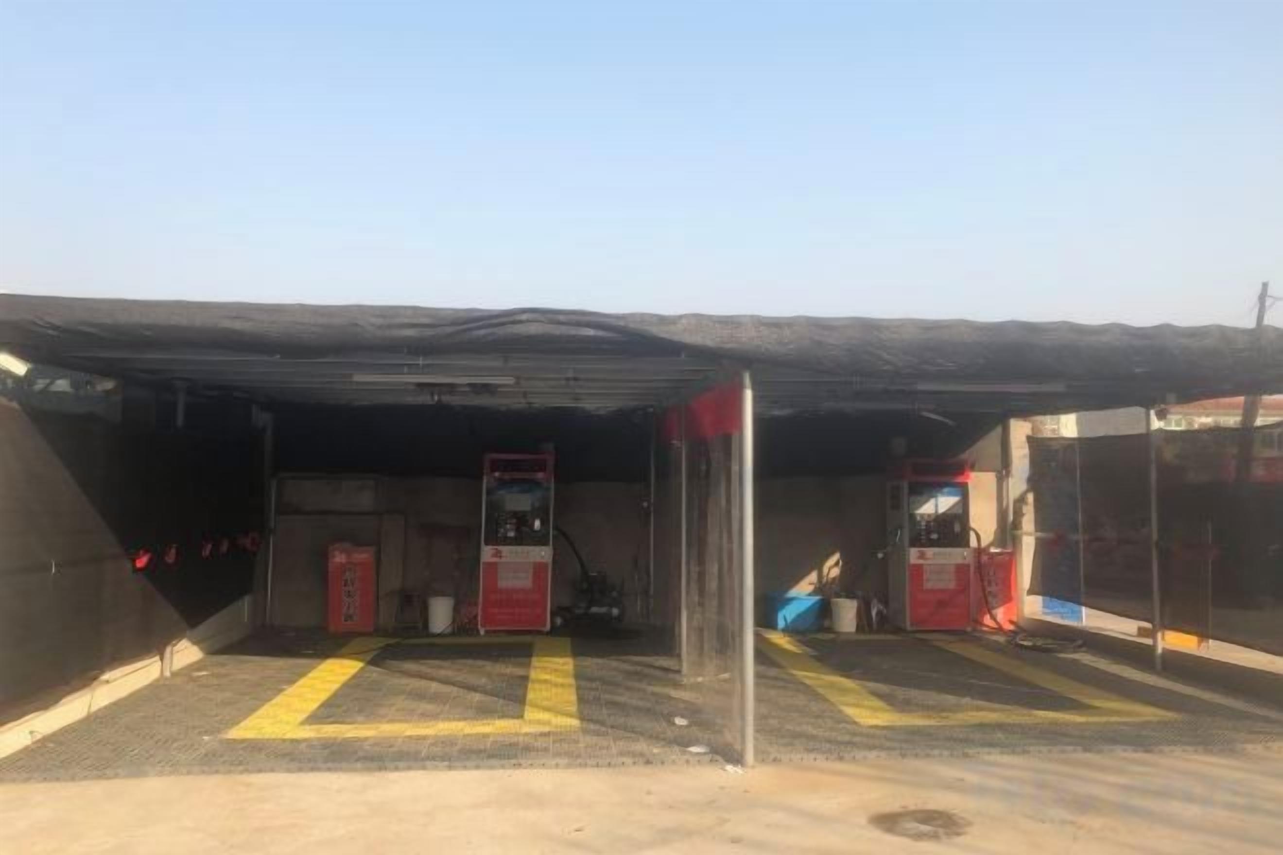 A covered parking area with a fuel pump, a fire extinguisher, and a red emergency phone.