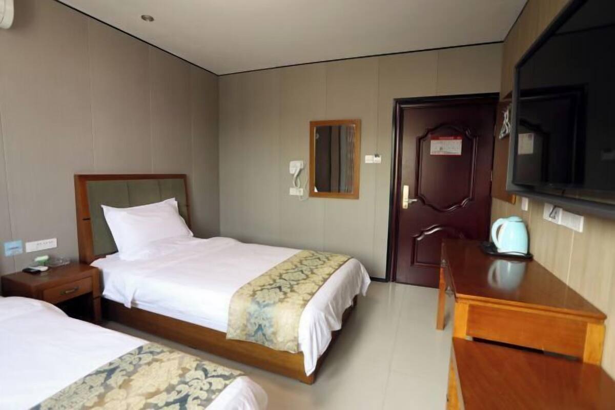 Une chambre d’hôtel avec deux lits, une table de chevet en bois, un bureau, une télévision et une porte avec une pancarte.