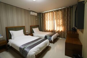 A hotel room with two beds, a wooden dresser, a TV, and a window with curtains.