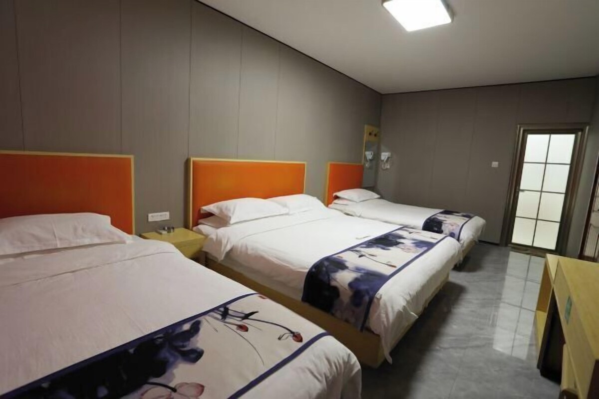 A hotel room with three beds, each with an orange headboard, white bedding, and floral-patterned blankets.