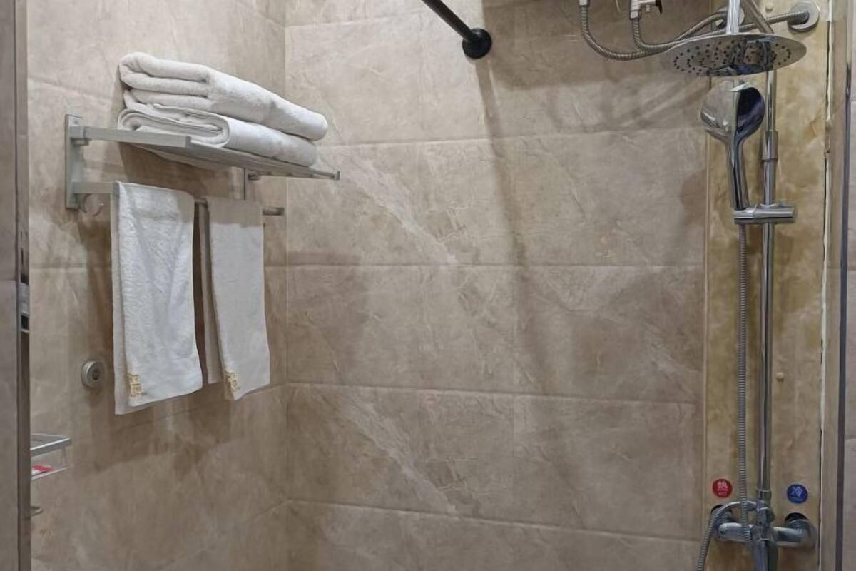 Un espace douche doté d’une porte en verre, d’un porte-serviettes avec des serviettes pliées et d’un pommeau de douche à main.