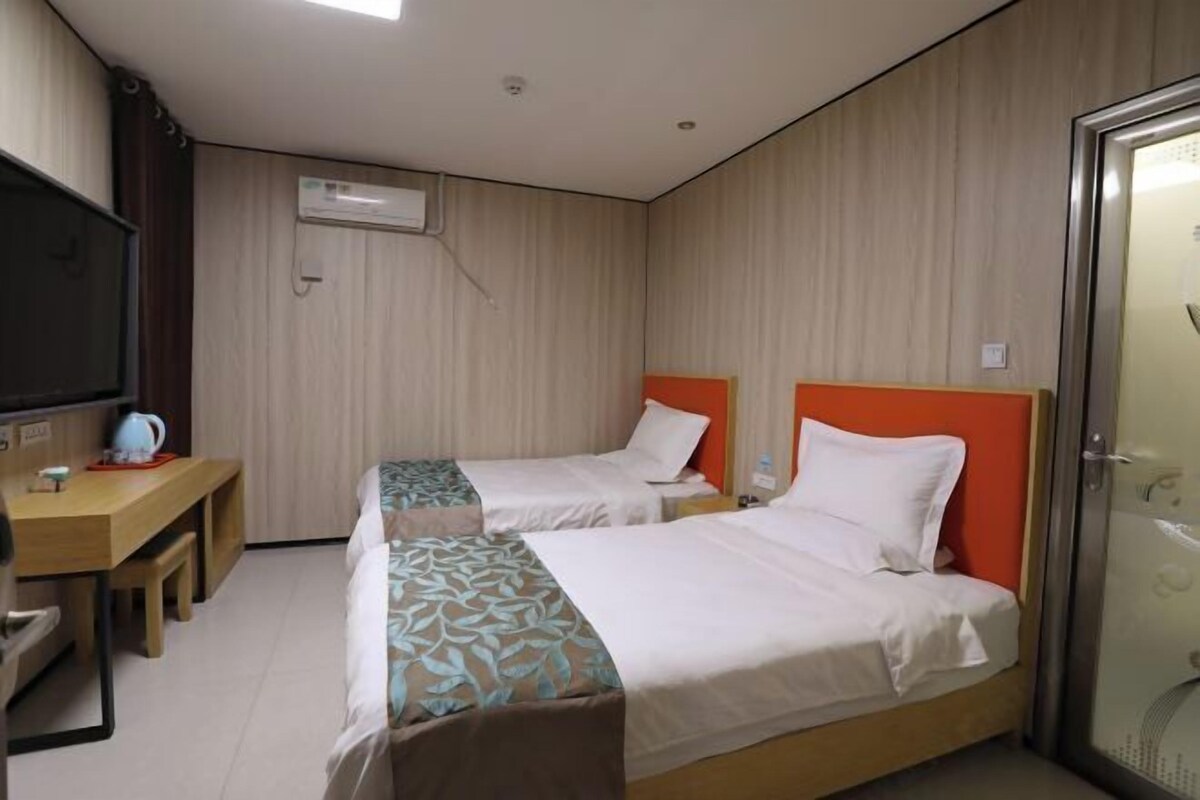 A hotel room with two beds, a desk with a chair, and a television.