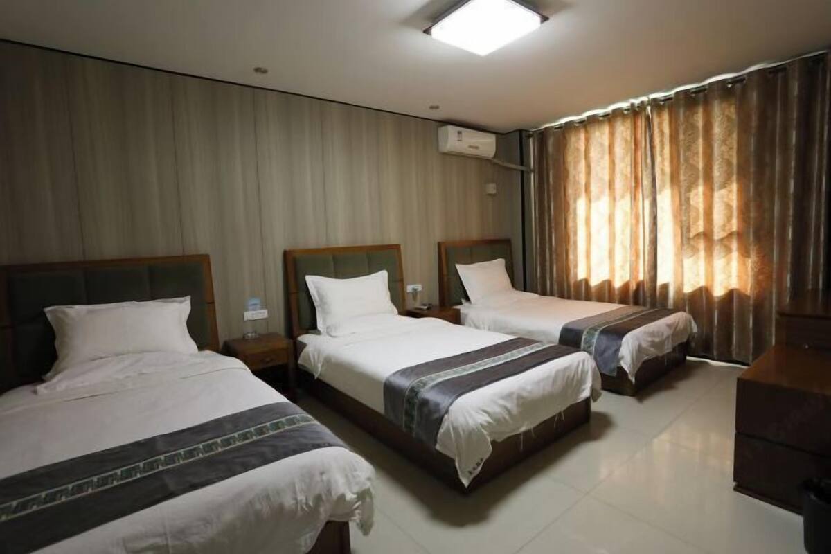 Une chambre d’hôtel avec trois lits, un téléviseur à écran plat, un bureau et une fenêtre avec des rideaux.