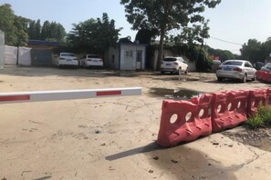 Un área de estacionamiento con una barrera roja, una entrada con portones y varios automóviles estacionados.