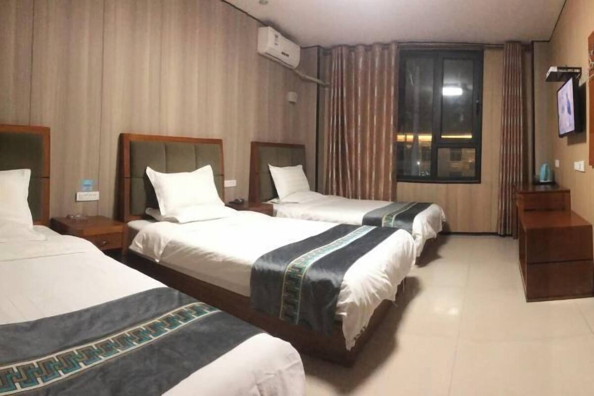 Une chambre d’hôtel avec trois lits, une télévision, un appareil de climatisation et une fenêtre avec des rideaux.