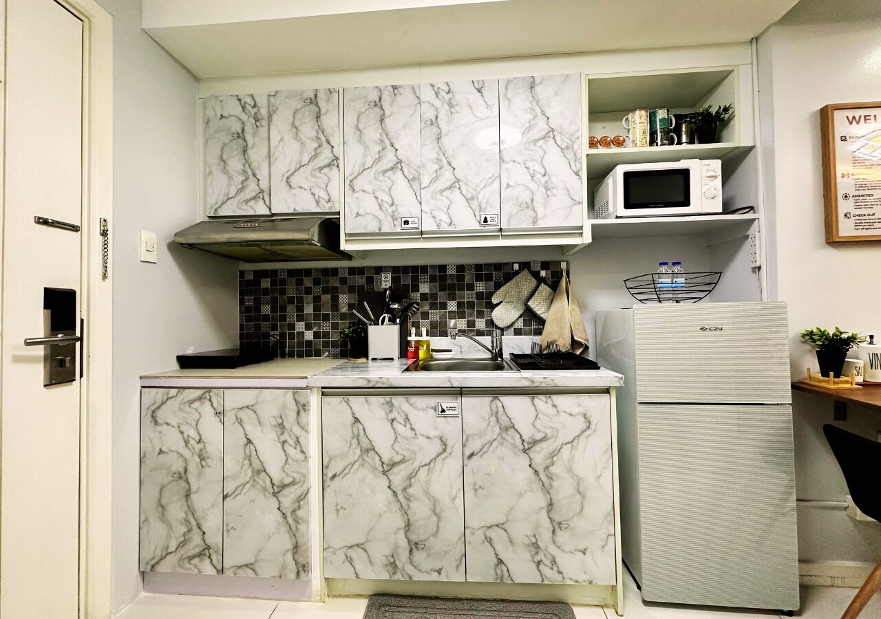 A compact kitchen with marble cabinets, a microwave, and a refrigerator.