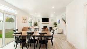 Un vaste espace de vie comprenant une grande table à manger, des sièges confortables, un téléviseur à écran plat et un escalier menant à un autre niveau.