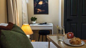 A room with a bed, a desk with a lamp, a painting, and a table with a glass of water and a croissant. - Spa Bath 20 Min to  Lincoln Financial Field + Dedicated Parking + City Access (Philadelphia)