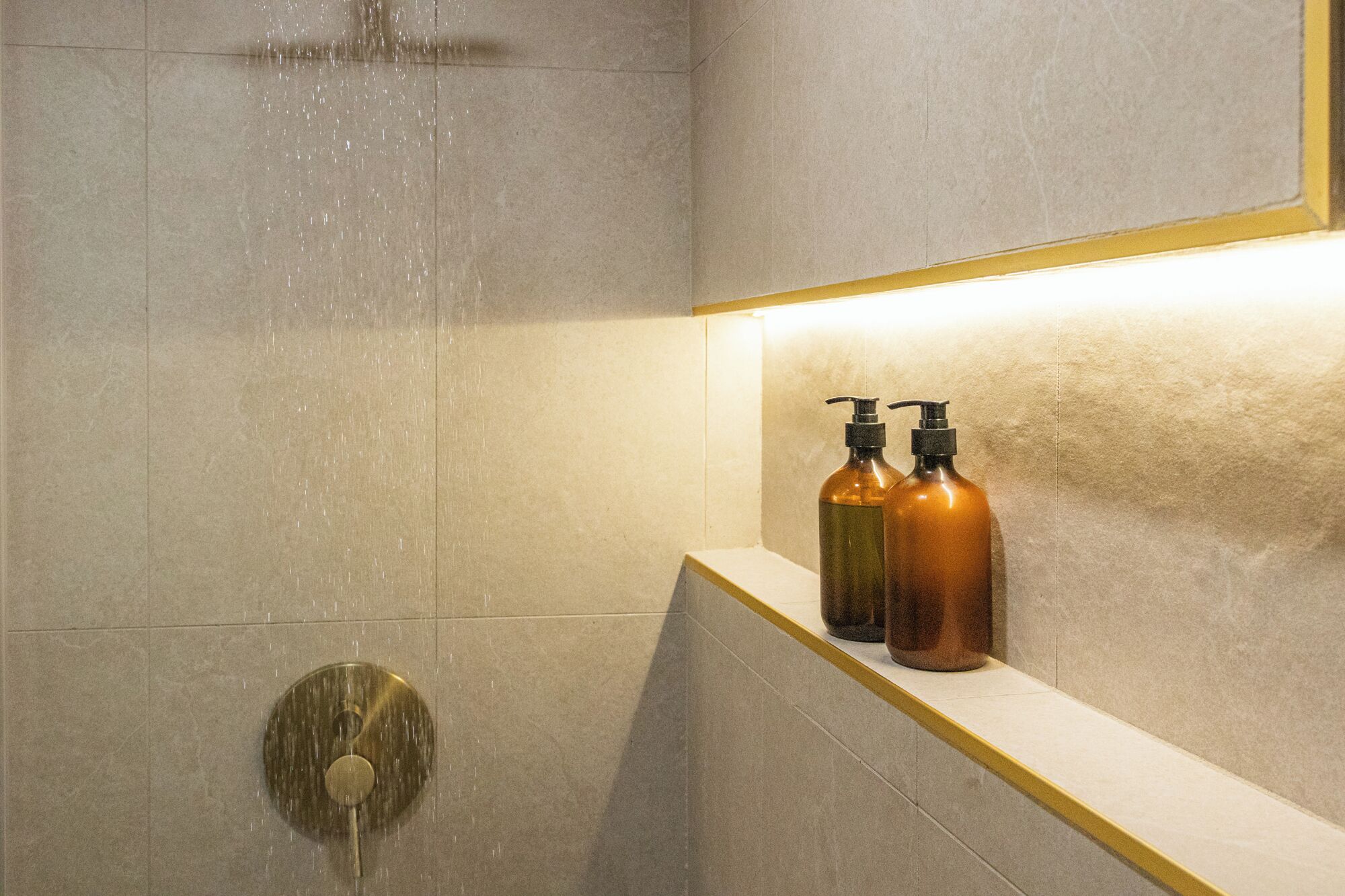 Eine Dusche mit Regendusche, einem runden Duschkopf und zwei Flaschen auf einem Regal.