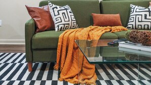A green sofa with patterned pillows, a glass coffee table, and a striped rug. - Spa Bath 20 Min to  Lincoln Financial Field + Dedicated Parking + City Access (Philadelphia)