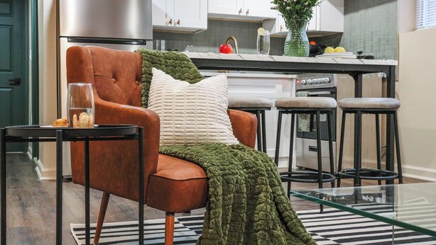 A modern kitchen with a dining area featuring a brown leather chair, a glass table, and a green knitted blanket. - Spa Bath 20 Min to  Lincoln Financial Field + Dedicated Parking + City Access (Philadelphia)