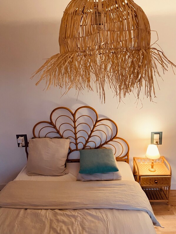 Un lit avec une tête de lit en osier, une lampe de chevet et une prise électrique sur le mur.