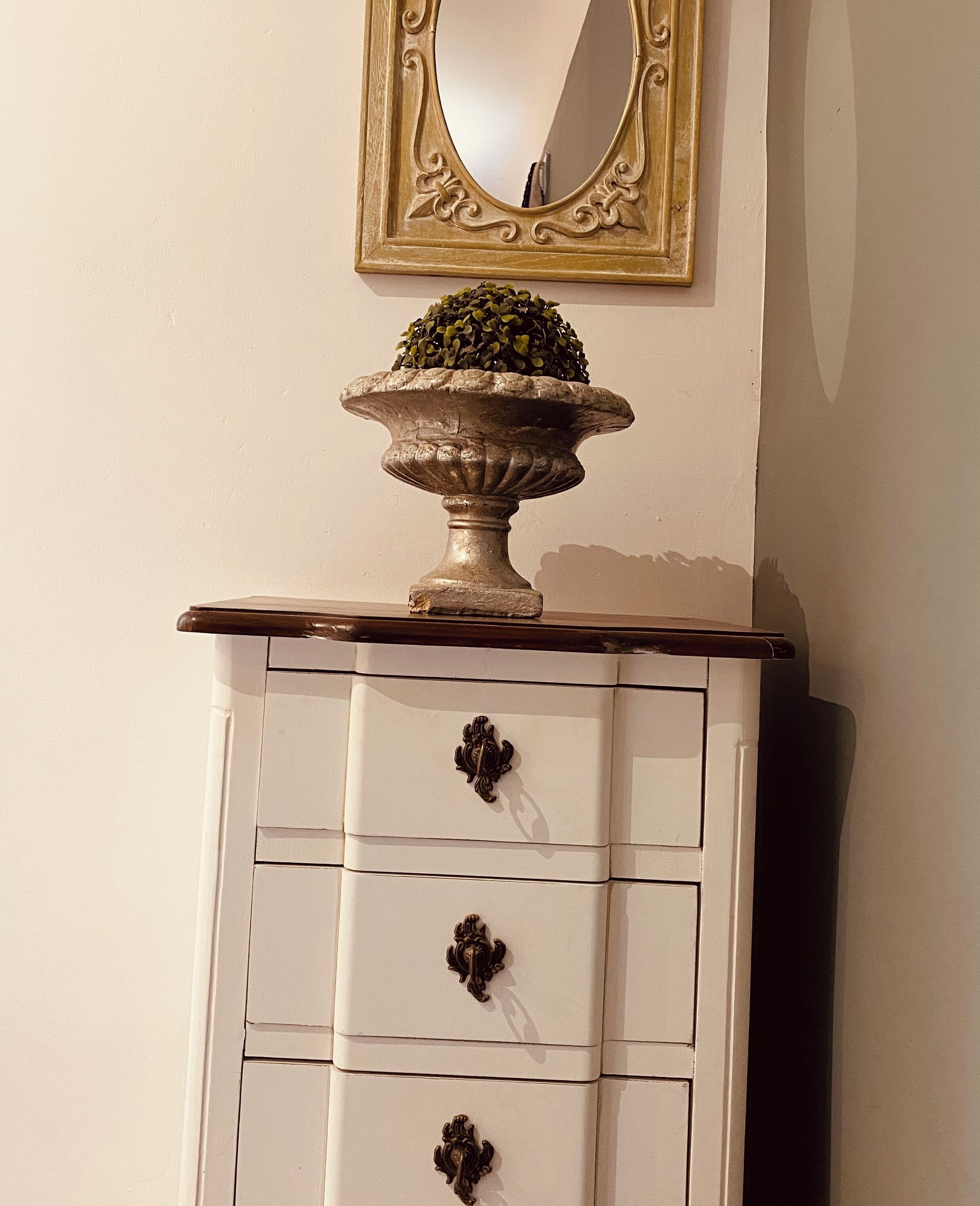 A white dresser with three drawers and a decorative urn on top.