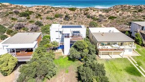 A modern coastal property with three detached houses, solar panels, and a view of the ocean.