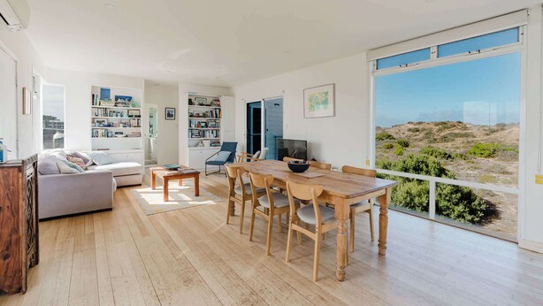 A modern living room with a dining area, large windows, and a view of the outdoors.