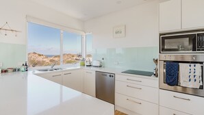 A modern kitchen with a large window, stainless steel appliances, and a view of the dunes.