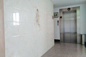 A hallway with a marble wall and an elevator.
