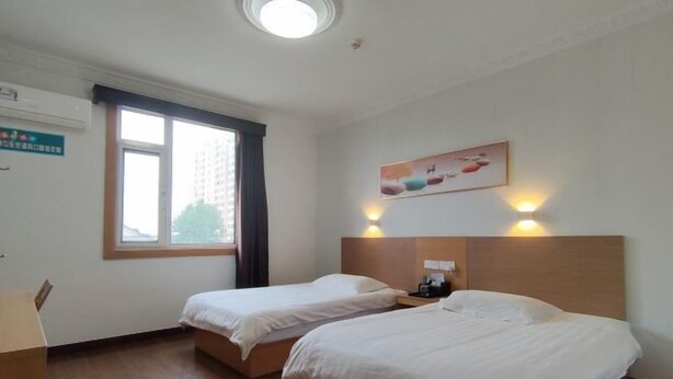 Una camera d'albergo con due letti, una scrivania e una finestra con tende.