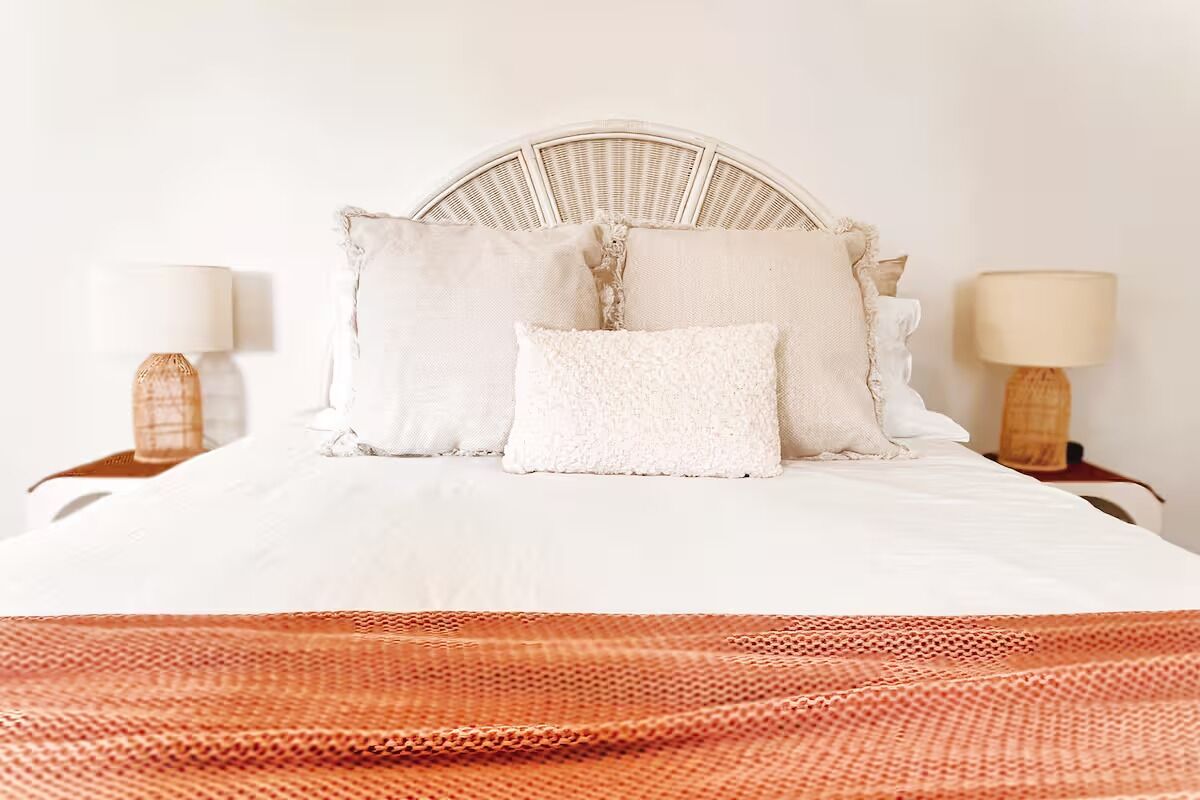 A bed with a white headboard, multiple pillows, and a red knitted blanket.