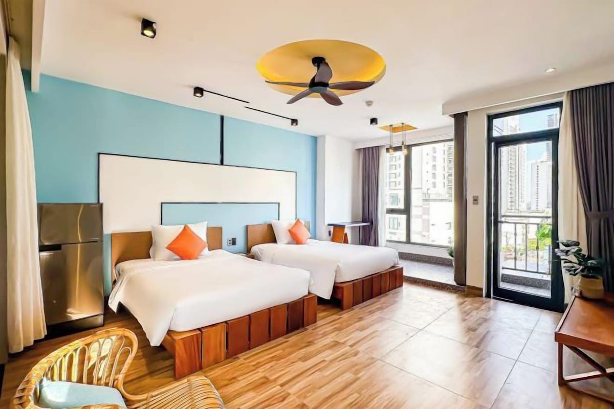 A hotel room with two beds, a ceiling fan, a large window, and a balcony.