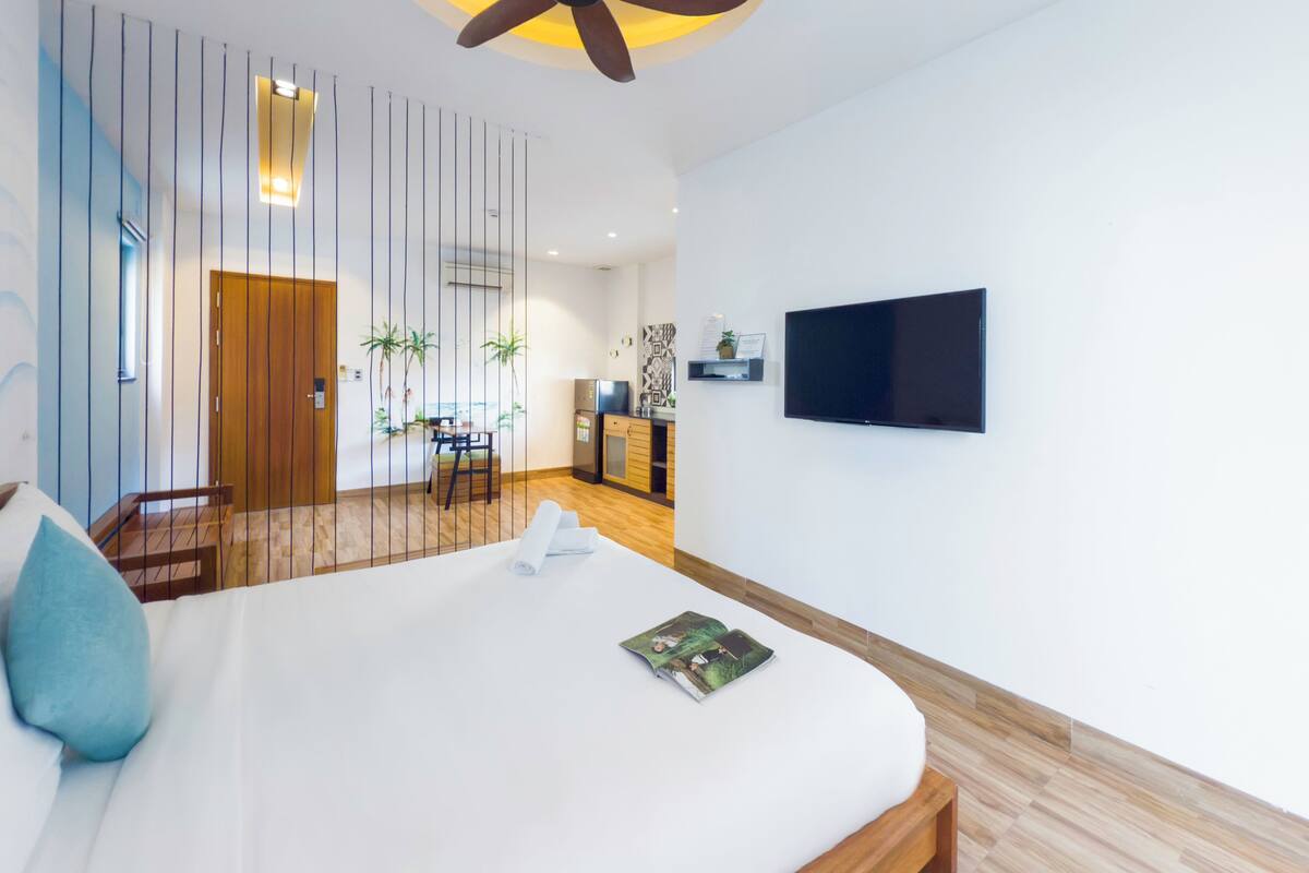 A modern hotel room with a large bed, a ceiling fan, a TV, and a view of the dining area.