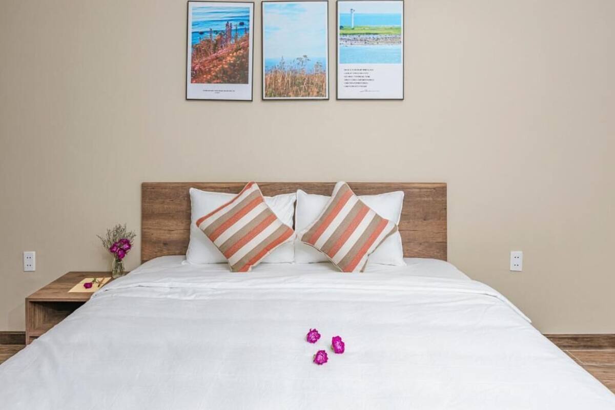 Una cama bien hecha con almohadas a rayas, un cabecero de madera y una mesita de noche con un florero.