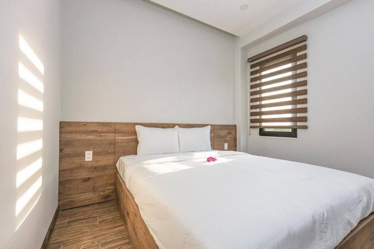 Un dormitorio con cabecera de madera, cama con ropa de cama blanca y una ventana con persianas horizontales.