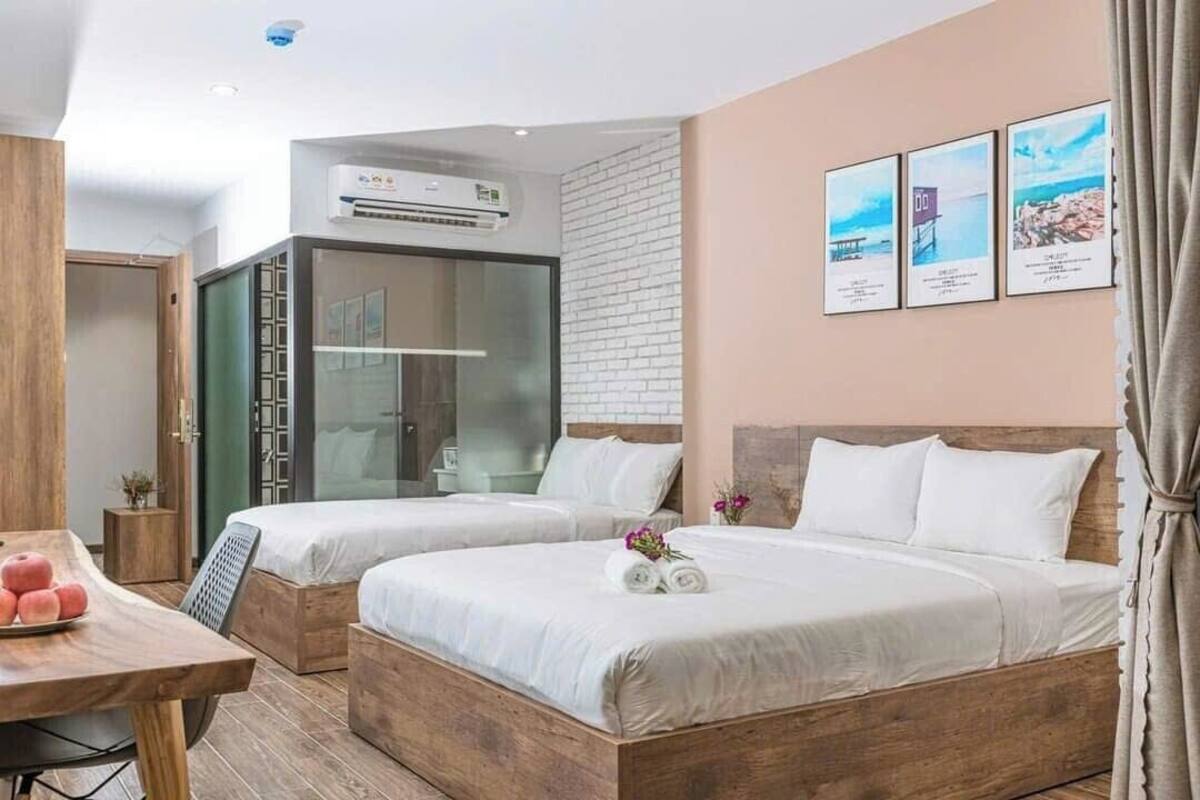 Habitación de hotel con dos camas, una mesa de madera con fruta, un armario y un baño con puerta de vidrio.