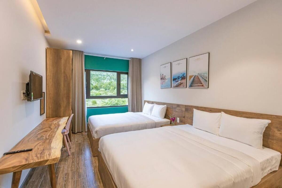 Habitación de hotel con dos camas, un escritorio de madera, televisión y un ventanal con vistas a zonas verdes.