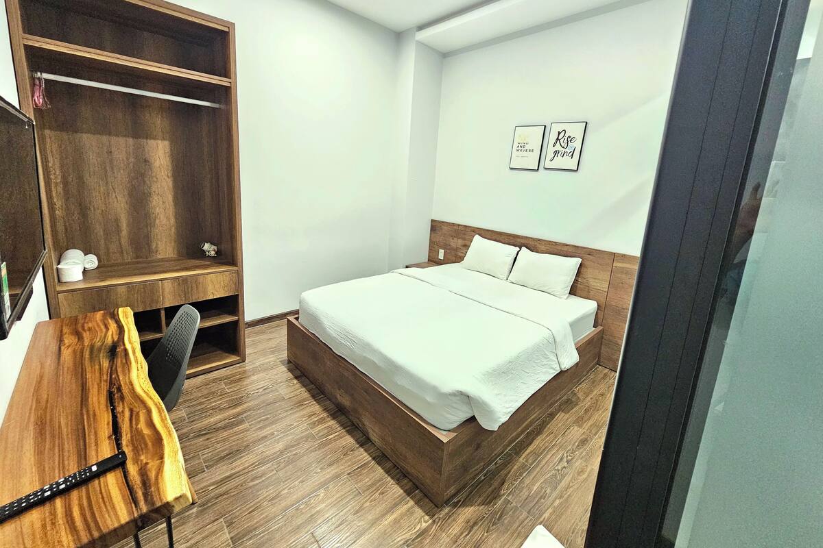 Un dormitorio con estructura de cama de madera, un escritorio con silla, un armario de madera y dos citas motivacionales enmarcadas en la pared.