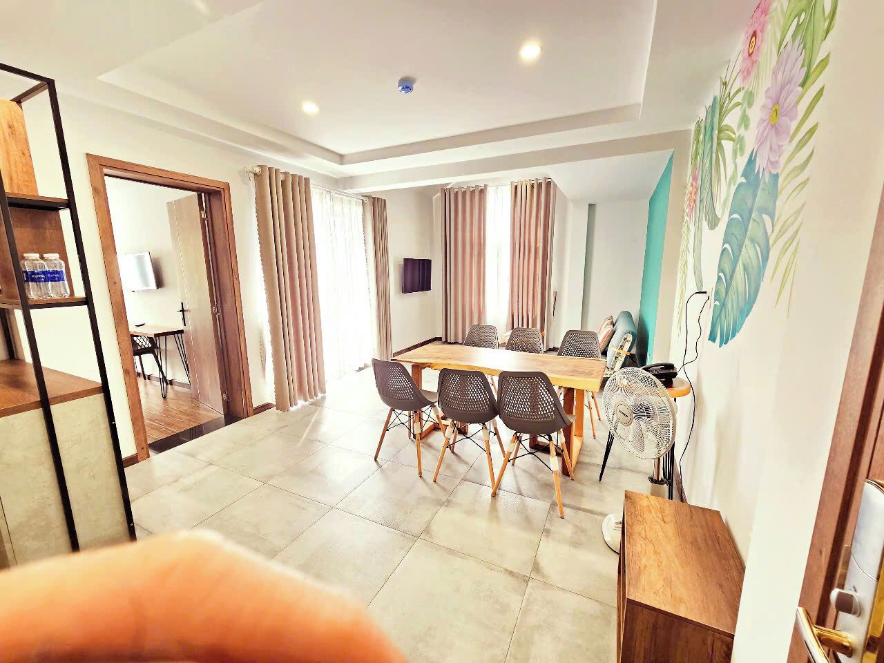 Une chambre d’hôtel moderne équipée d’une grande table à manger, de plusieurs chaises, d’un téléviseur et d’un ventilateur.