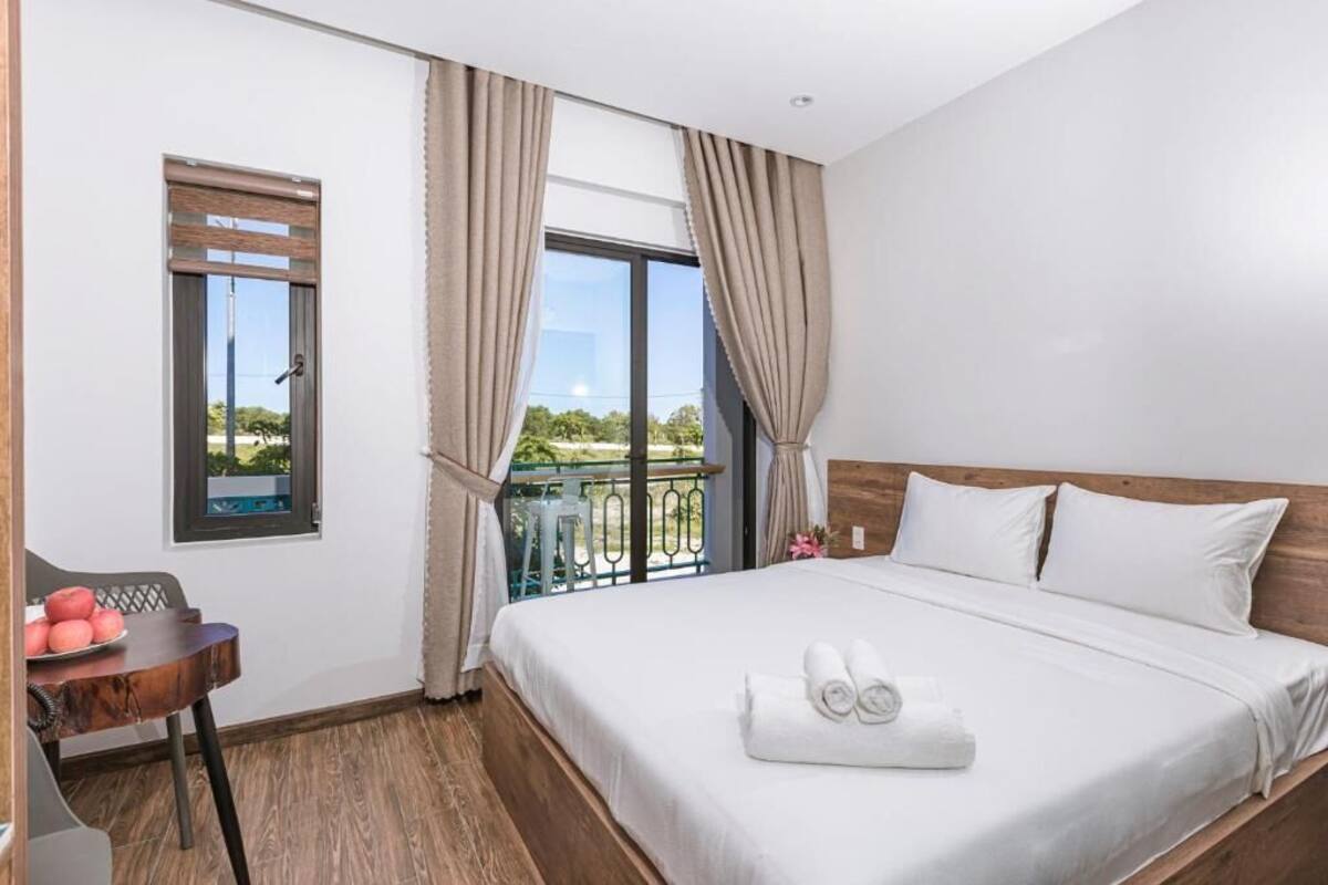 Habitación de hotel con una cama, una mesita con manzanas, un ventanal con cortinas y un balcón con vistas.
