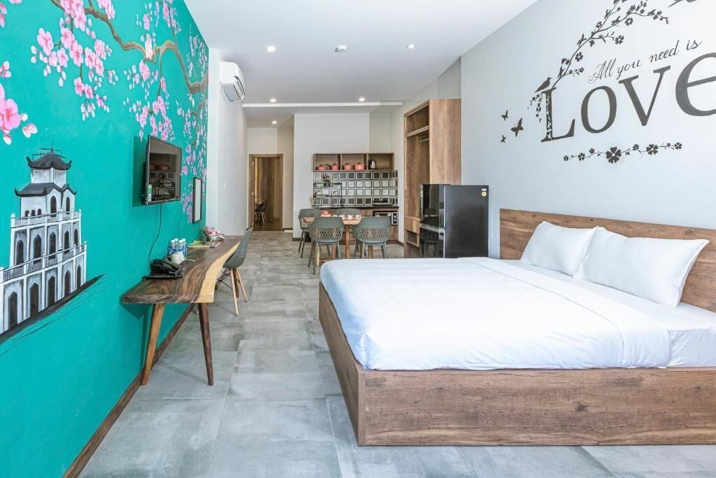 A bedroom with a wooden bed, a desk, and a chair. There is a wall with a mural and a shelf with items.