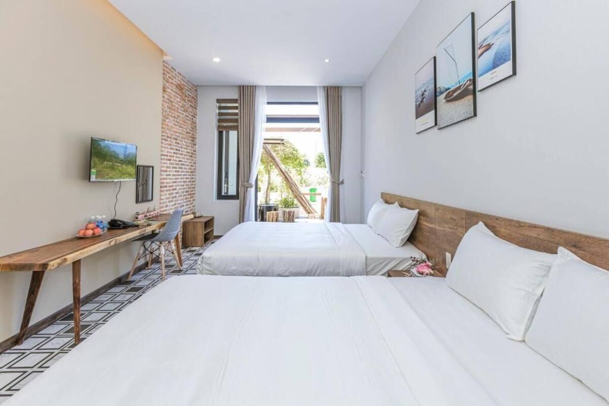 Habitación de hotel con dos camas, un escritorio con silla, televisión y balcón con vistas a zonas verdes.