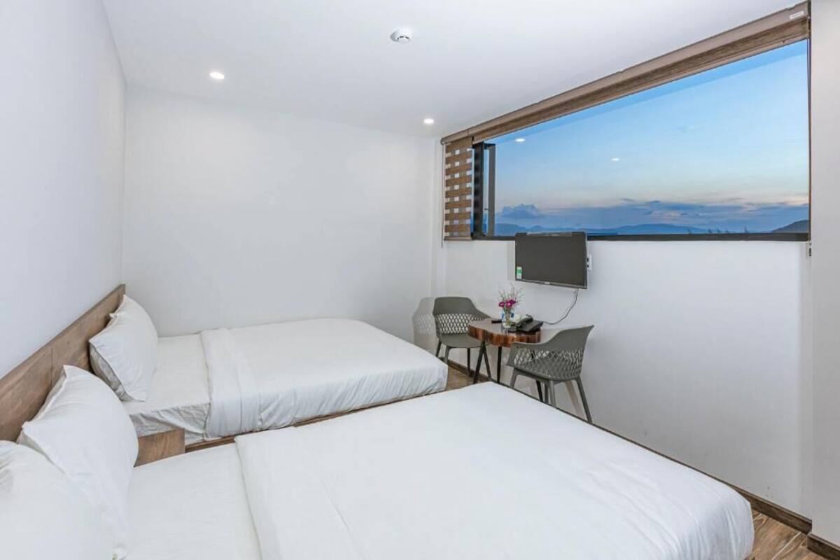 Habitación de hotel con dos camas, una mesita con sillas, televisión y una ventana grande con vistas a la montaña.