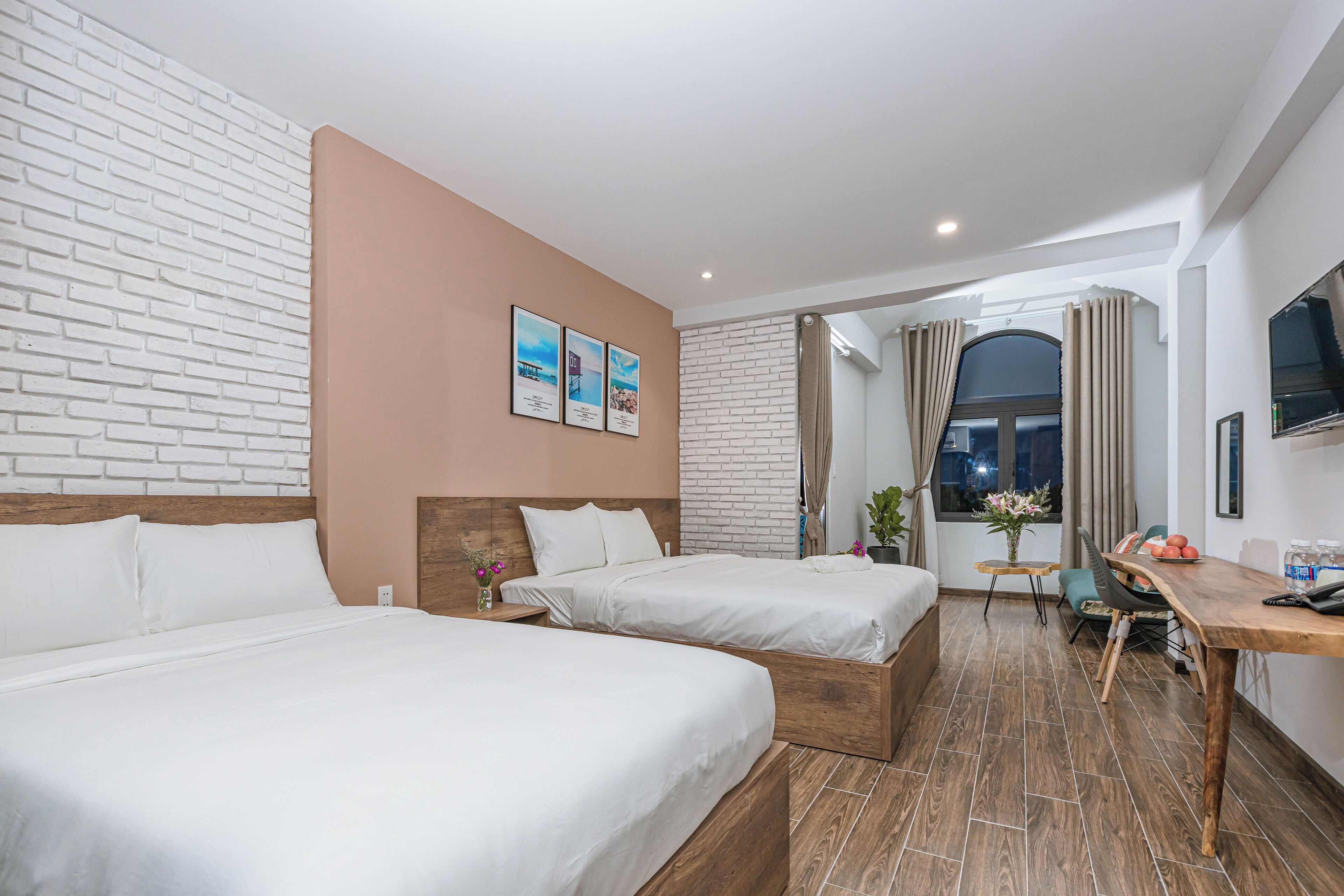Une chambre d’hôtel avec deux lits, un bureau en bois, une télévision et une fenêtre avec des rideaux.