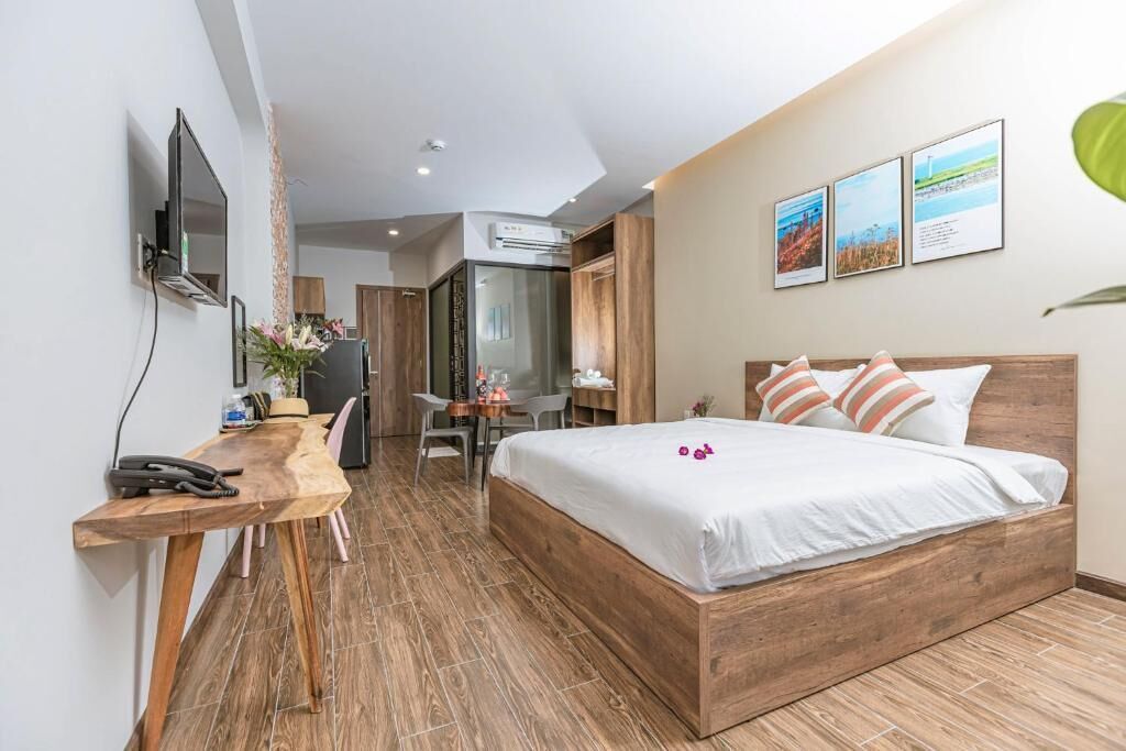 Une chambre d’hôtel moderne avec un lit en bois, un bureau avec une chaise, un téléviseur fixé au mur et une petite table avec une plante.