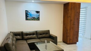 A modern living room with a sectional sofa, a glass coffee table, and a wooden cabinet. - The Good Vibes by Aero Stays (Kasauli)