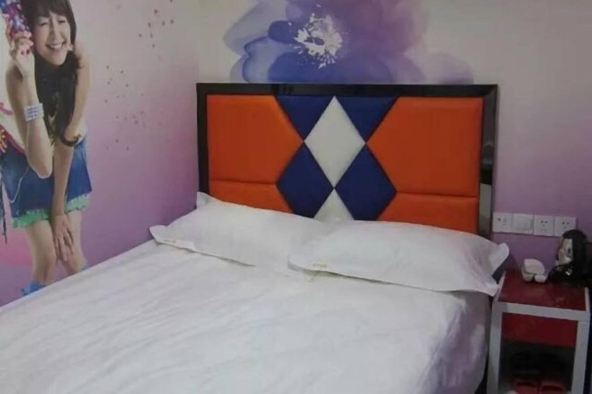 A bed with a diamond-patterned headboard, a white pillow, and a nightstand with a phone and a small figurine.